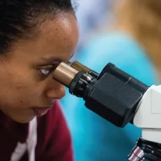 A woman examining a specimen under a microscope.